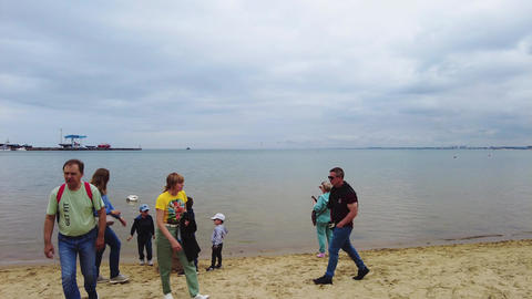 People rest on the sandy shore of the Black Sea next to white swans. 0165 1