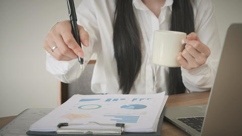 Female manager holding cup of coffee and writing on document, check financial