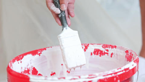 Close up of white paint dripping from a brush, process of preparing to paint