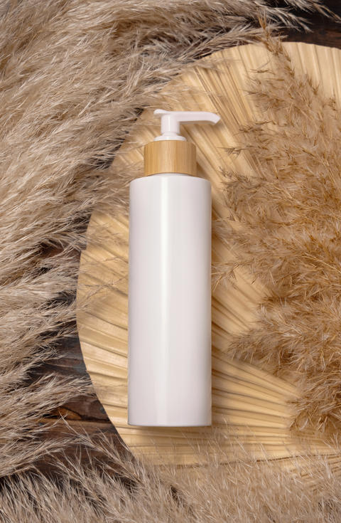 White Cosmetic one pump bottle on palm leaf near pampas grass to