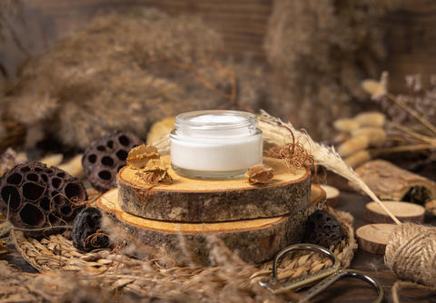 Opened glass cream jar on wood near natural decorations close up