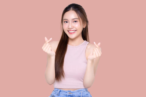Beautiful young Asian woman shows mini heart fingers on isolated pink background