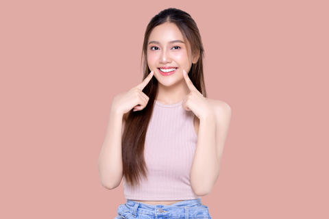 Beautiful young Asian woman pointing finger to her teeth on isolated pink background