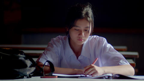 Asian female student sitting and doing exercises waiting for her parents to come take her home