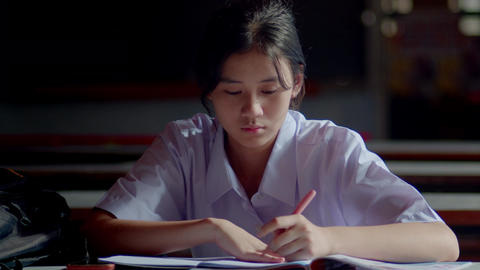 Asian female student sitting and doing exercises waiting for her parents to come take her home