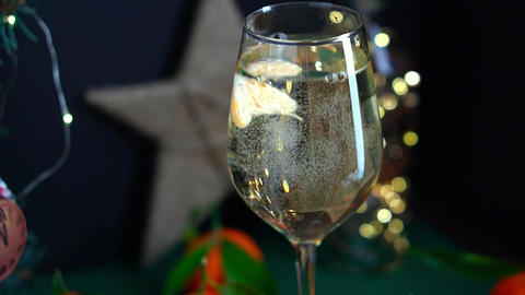 Tangerine slices pouring in wineglass fuul of sparkling wine on table with
