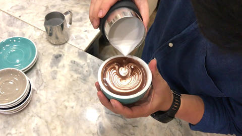 Video of the barista is pouring lily flowers latte art pattern on a hot mocha coffee