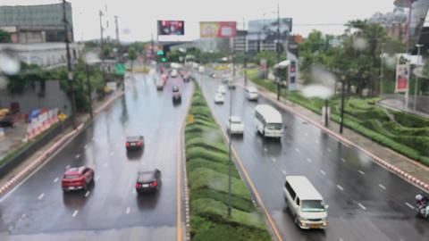 shot through glass window with raindrops showing many cars driving on the road