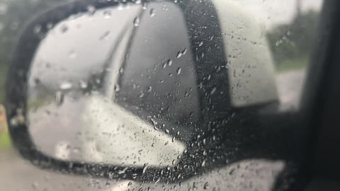 view from the left side mirror while the white car is driving on a rural road in the rain