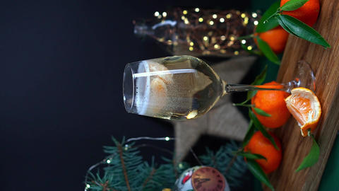 Tangerine slices pouring in wineglass fuul of sparkling wine on table with