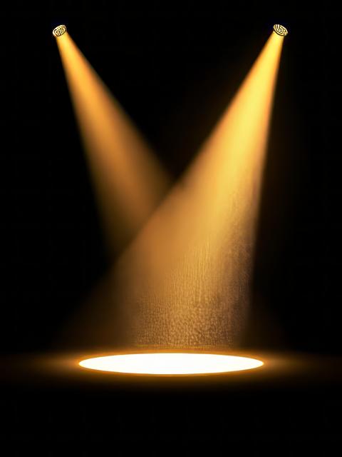 Spotlight shines down from the top of empty stage creating a golden light effect on a black