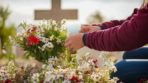 Woman arranging flowers on grave in cemetery with cross