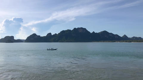 Sunny Thailand seascape with boat gliding across calm waters and mountains in the background