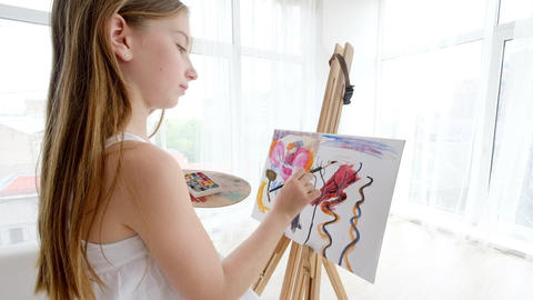 Little girl painting on easel in art studio