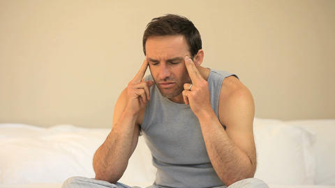 Man having a headache sitting on the bed