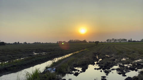 A vast open farmland with ponds and clear skies at sunset or sunrise