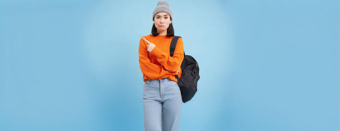 Skeptical asian woman pointing left at strange banner, looks doubtful, stands over studio background