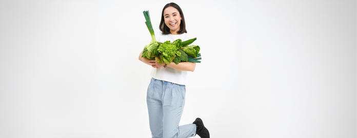 Image of smiling asian woman, vegetarian with lots of green vegetables, eating oranic food, isolated