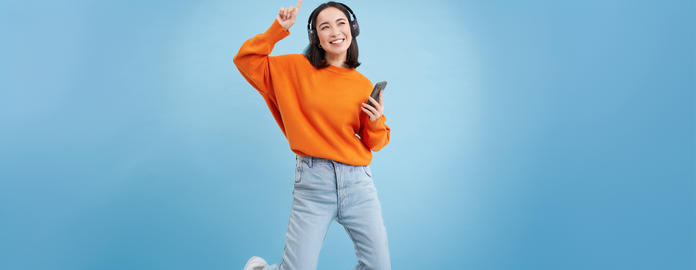 Beautiful korean woman in headphones, dancing, listening music on mobile phone app, smiling, posing