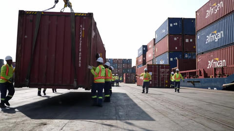 Workers manage cargo containers at busy shipping terminal during daylight hours