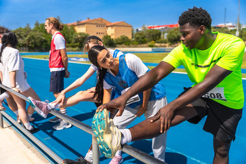 Athletes stretching legs on track and field, preparing for competition
