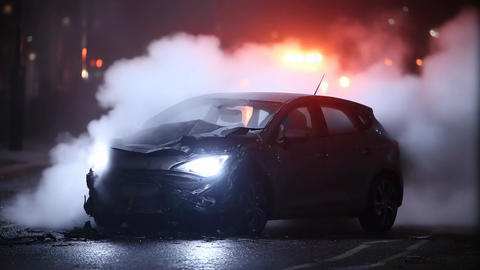 Sudden car accident at night with smoke rising from damaged vehicle in urban setting