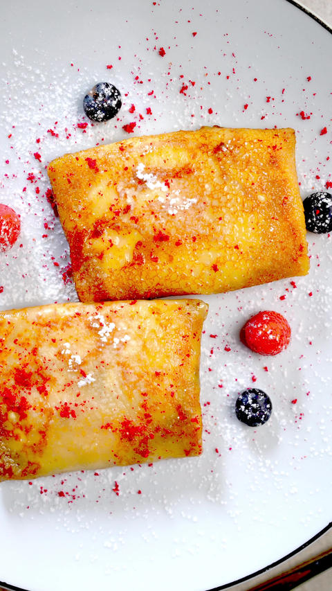Ukrainian nalysnyky filled with wild forest berries, dusted with powdered sugar, drizzled with zesty