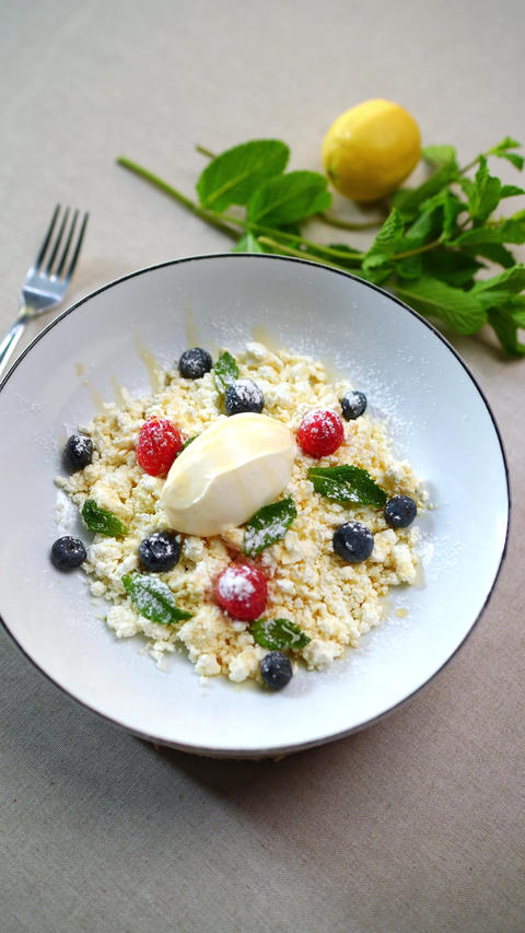 Cottage cheese dessert drizzled with honey, garnished with mixed berries, mint leaves, lemon zest