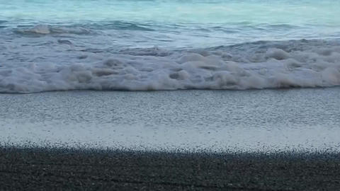 Coastal waves roll onto the sandy shore and spread over the sand
