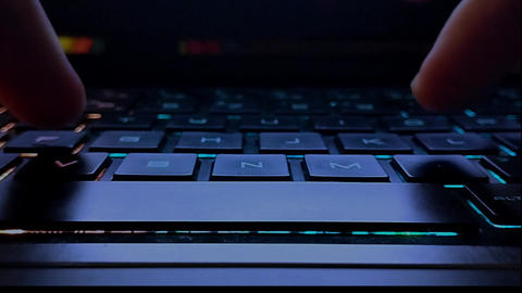Hands typing on the English keyboard of a laptop with multi-colored backlight