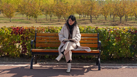 Woman Reading a Book on a Park Bench in Autumn