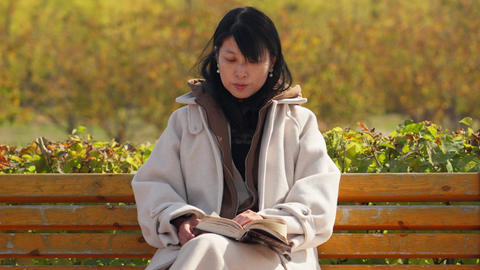 Woman in Cozy Coat Reading on Park Bench in Autumn