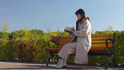 Woman in Cozy Coat Reading on Park Bench in Autumn