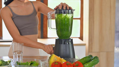 Smiling woman preparing a healthy green smoothie in a blender in a kitchen