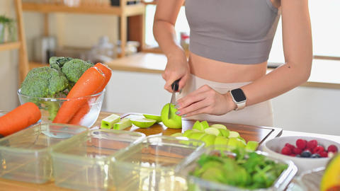Young woman slicing green apples on a cutting board surrounded by fresh fruits