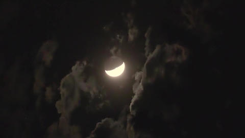 Crescent moon in the first quarter phase is hidden behind clouds in the night's black sky