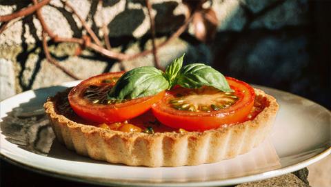 Sunlit Tomato Basil Tart With Flaky Crust On White Plate, Rustic Garden Wall And Bronze Ivy Elegant