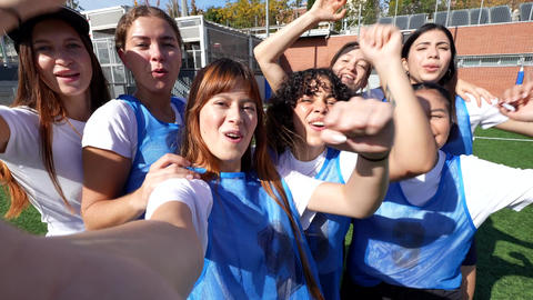 Excited female soccer players celebrating victory taking a selfie video on the field