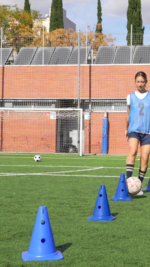 Female soccer players dribbling the ball through cones during training session