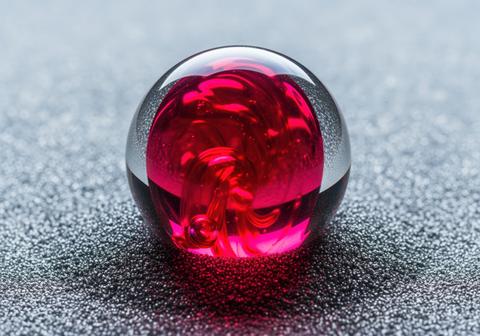 Macro shot of a transparent glass sphere with abstract red swirl on a dark textured background