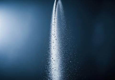 Slow motion cascade of shimmering silver dust falling through a dramatic light beam