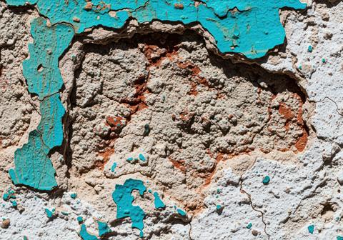 Abstract macro texture of peeling turquoise paint on a rough, cracked, and aged stucco wall