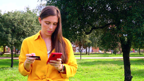 Young woman shopping online with credit card and smartphone outdoors copy space