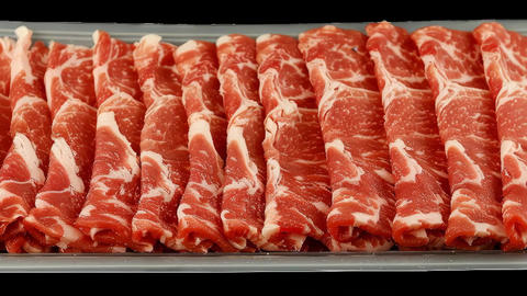 Thin slices of marbled beef are displayed on a tray, perfect for hot pot or shabu shabu, the raw