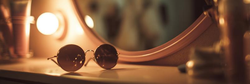 Stylish Sunglasses Resting on a Counter Near a Mirror With Warm Light