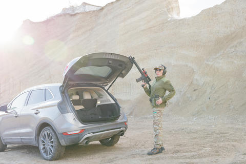 Female Soldier Holding Shotgun near Car with Open Trunk in Desert Area