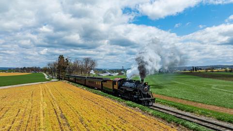 Locomotive Steam Train Travels Through Vibrant Fields on a Sunny Day in the