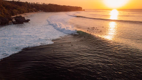 Surfers on Padang Padang surf spot on evening at sunset with perfect waves