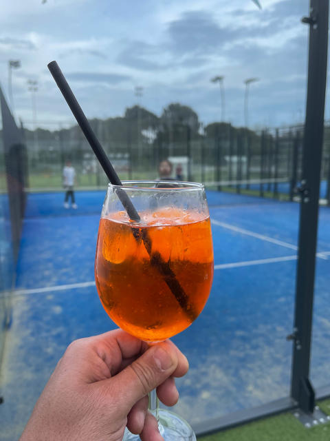 Red Spritz cocktail in a glass on a blue tennis court