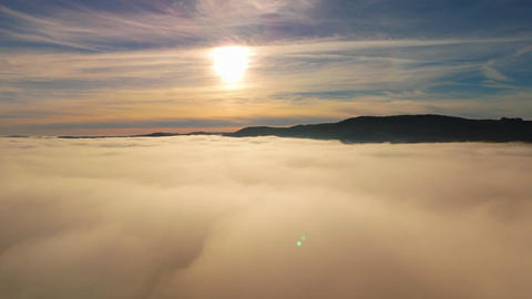 Sun above a sea of fog and clouds with mountain ridge under blue sky aerial view of foggy mountains